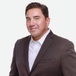 Headshot of Manny Barreras wearing a suit and smiling.